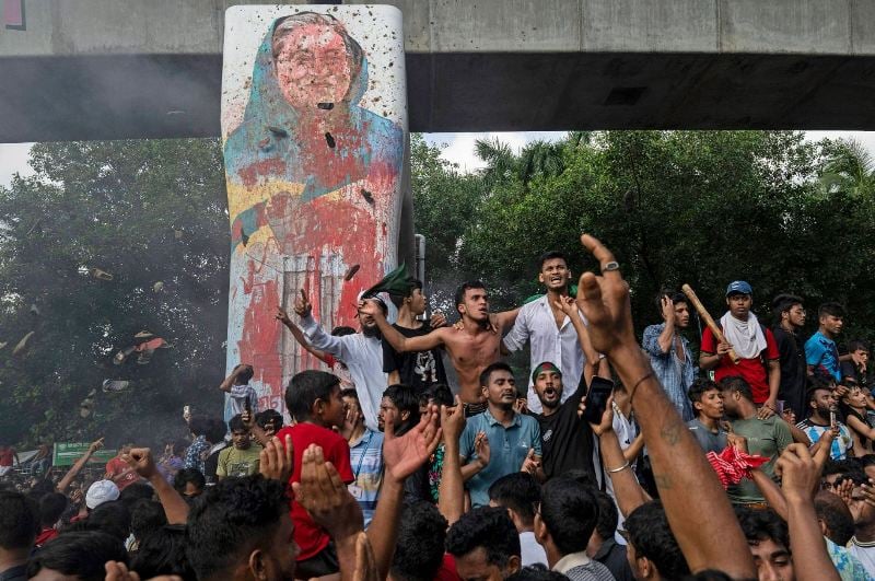5 August 2024: Protestors while celebrating beside a defaced portrait of Sheikh Hasina in Dhaka, Bangladesh, after she resigned from her post of Prime Minister