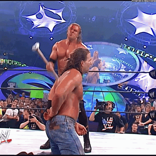 This may contain: two men wrestling in front of an audience with one holding a baseball bat and the other throwing a ball