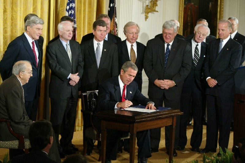 Biden with other politicians standing next to President Bush who is signing the Iraq War declaration