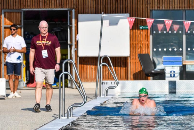 Bob Bowman (standimg right along the pool side) watching while Léon Marchand practising in the pool