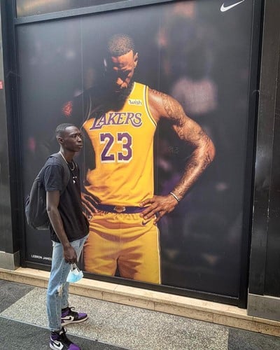 Khaby Lame posing in front of a poster of LeBron James