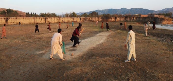 Noor Ahmad (bowling) playing cricket with his friends in his village