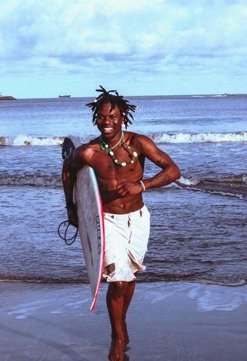 Rema on the beach with a surfboard
