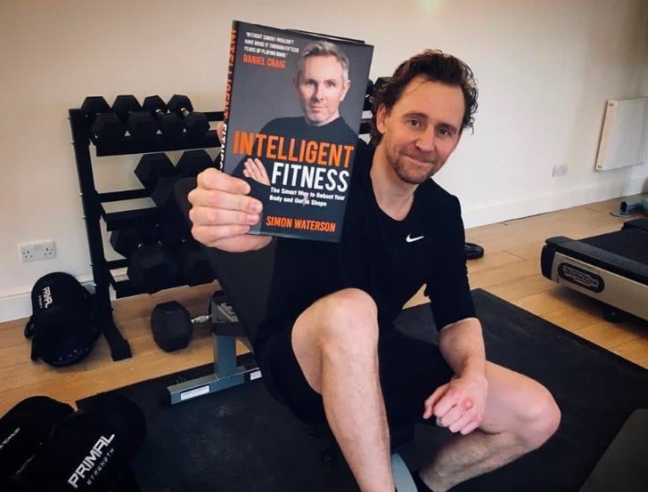Tom Hiddleston posing with a fitness book at a gym